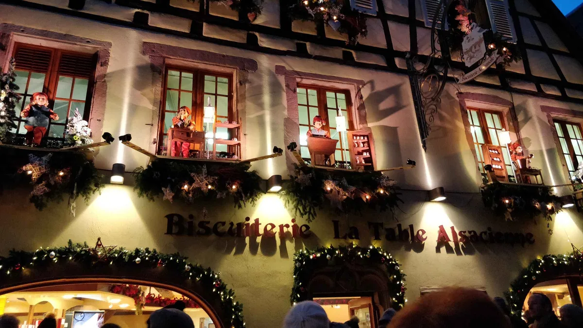 A half-timbered shopfront in Alsace at night, its balconies decorated with Christmas figures, garlands and warm lights
