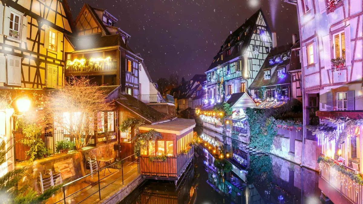 Colmar's Petite Venise at night, canal houses lit in purple and gold light reflected in the water