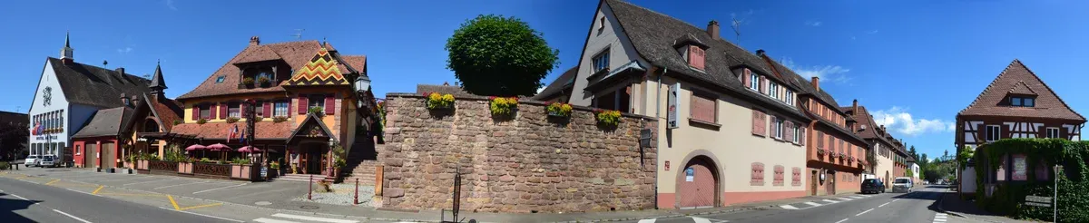 Panorama of half-timbered houses and a stone wall along the main road in Mittelwihr