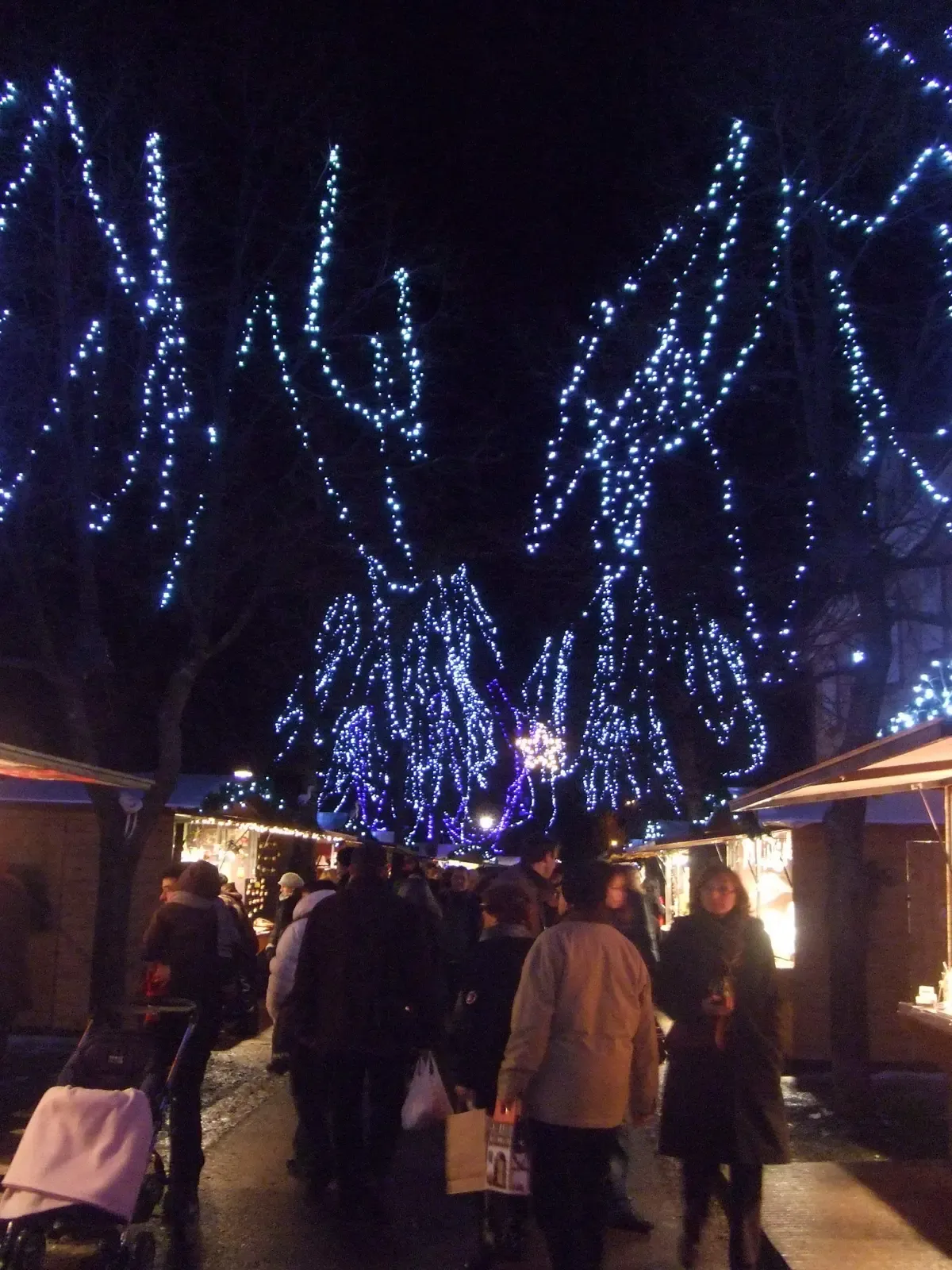 Blue light garlands over market chalets and visitors in Riquewihr at night