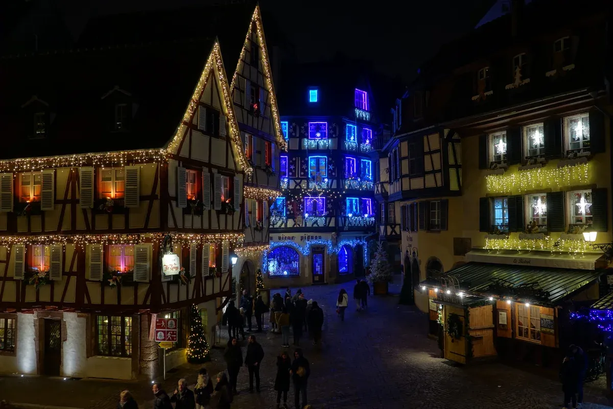 Half-timbered houses lit with Christmas lights on a Colmar street at night