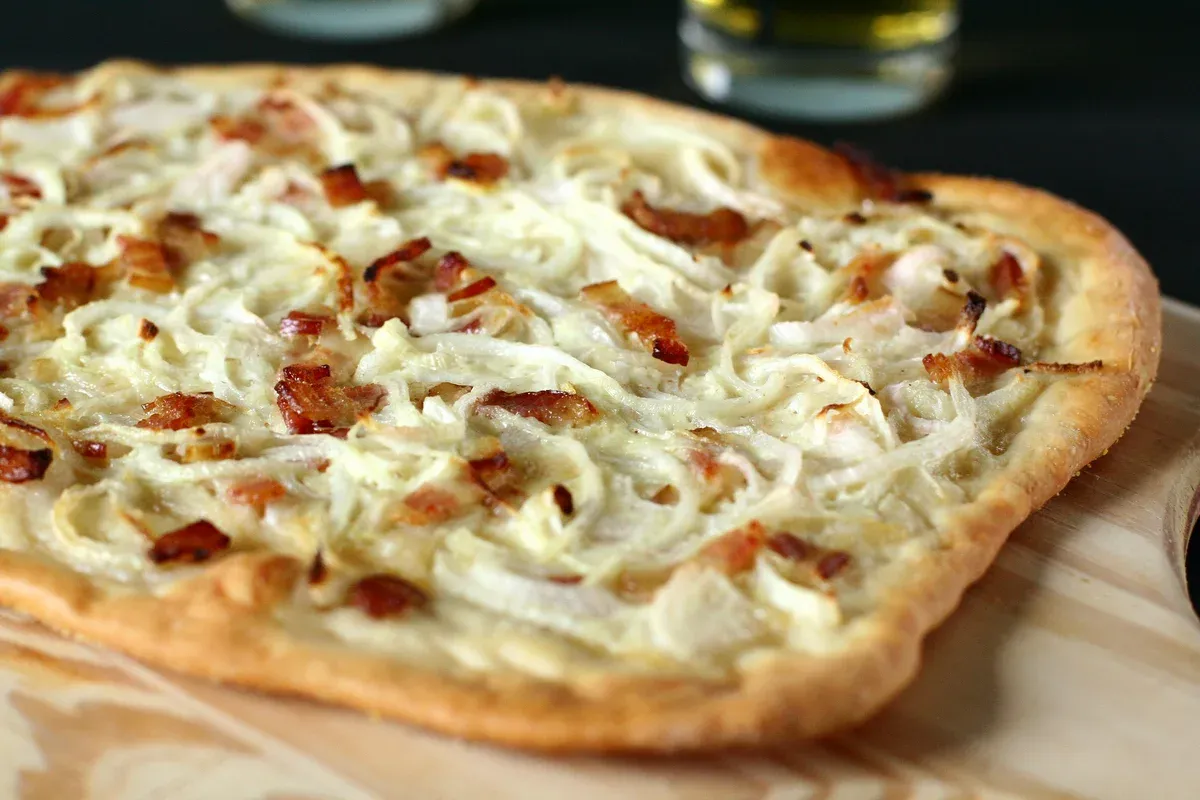 Tarte flambée topped with onions and bacon on a wooden board